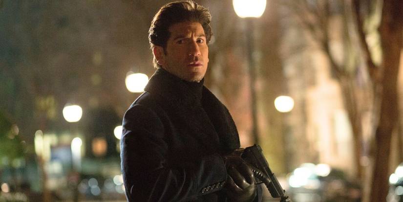 Jon Bernthal as Brax, wearing a jacket and clutching a pistol in the city streets in The Accountant.