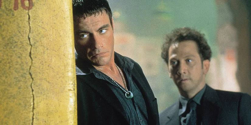 Jean-Claude Van Damme and Rob Schneider taking cover behind a yellow wall in the film Knock Off (1998)