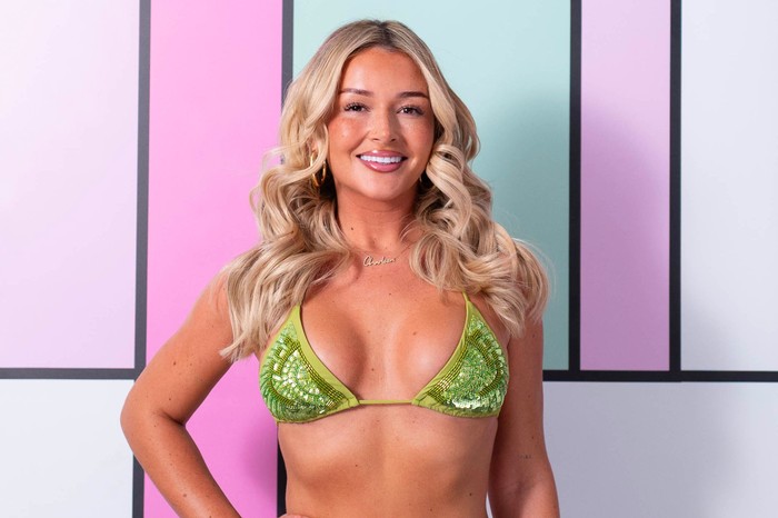 Love Island S13 Charleen posing in front of the Love Island background, wearing a sparkly green bikini. She has blonde hair and is smiling, with her hand on her hip.