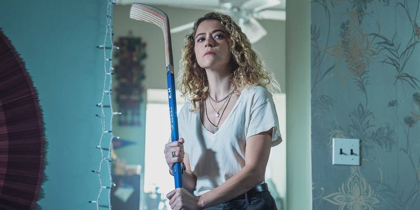 Tatiana Maslany holds a hockey stick and searches her home in 'Maximum Pleasure Guaranteed' image