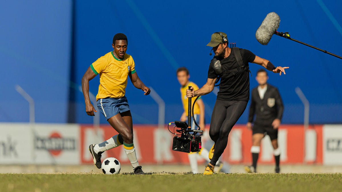A camera crew captures soccer action for the series Brazil '70: The Third Star. A cameraman captures a soccer player with others in the background.