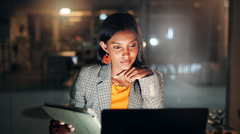 A woman thinking while using a computer and a tablet in a dark office