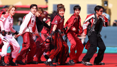BTS in coordinated red and black outfits dancing energetically on a red stage.
