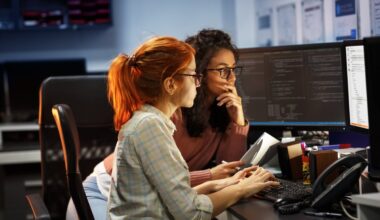 Two computer programmers working together while looking at computer screens.
