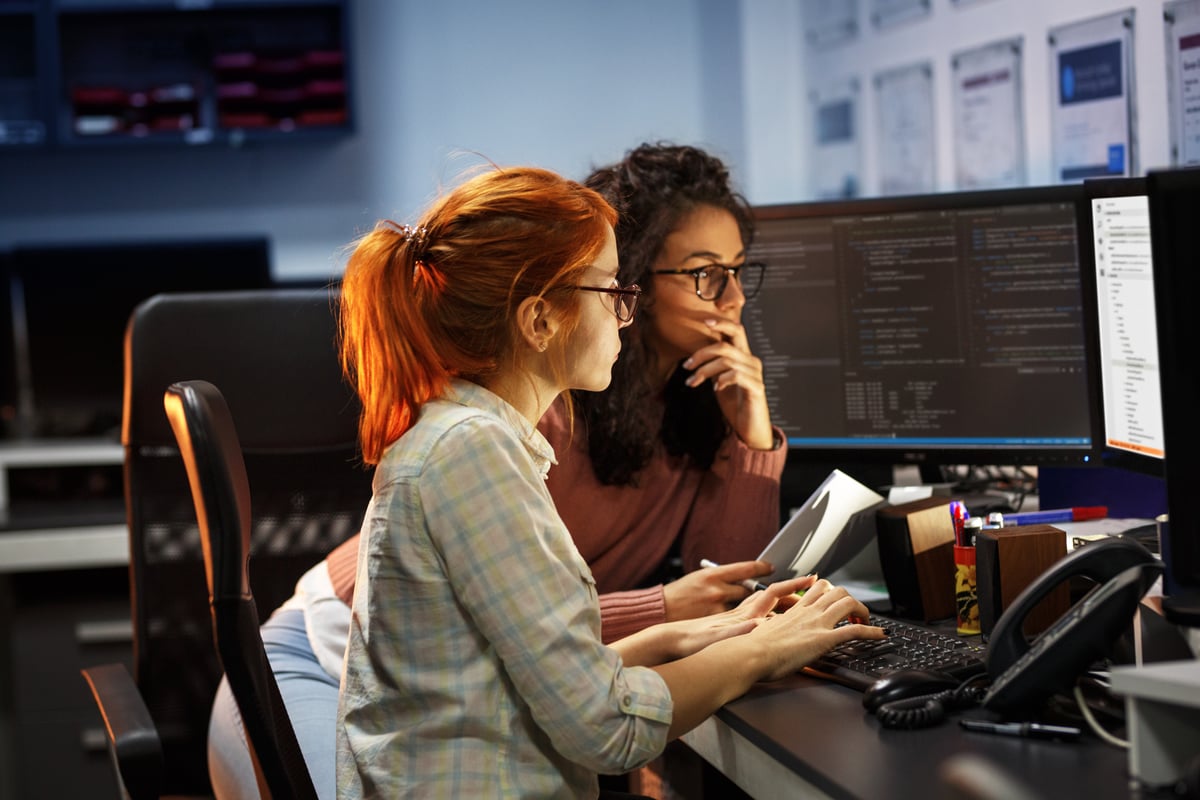 Two computer programmers working together while looking at computer screens.