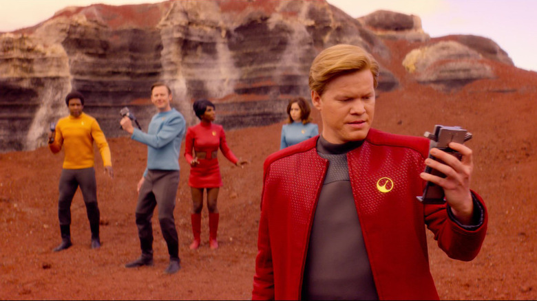 Jesse Plemons' Robert Daly checking on a device while crew members stand on the background on Black Mirror