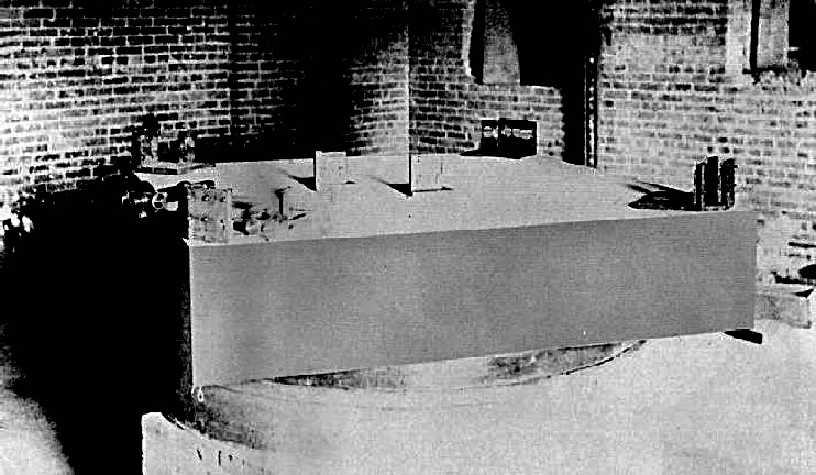 A black and white photo of a rectangular prism device in a brick wall room.