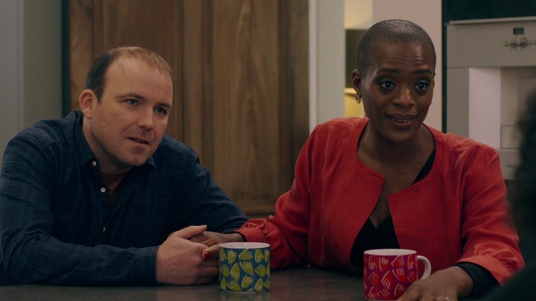 Stephen and Celeste sitting at a table and holding hands on Years and Years S1E1