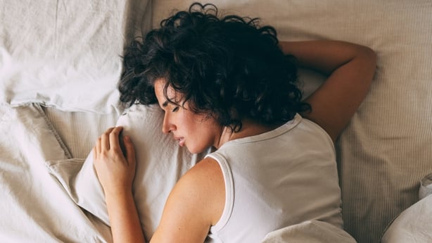 A woman with curly hair peacefully sleeping in a cozy bed, showcasing relaxation and restfulness. Perfect representation of comfort and tranquility for a restful night.