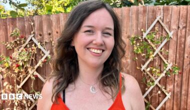 A white woman with brown hair smiles in the garden looking at the camera.