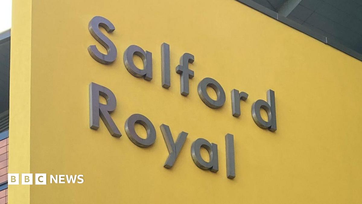 The Salford Royal Hospital sign. It is grey text emblazoned upon a yellow background.