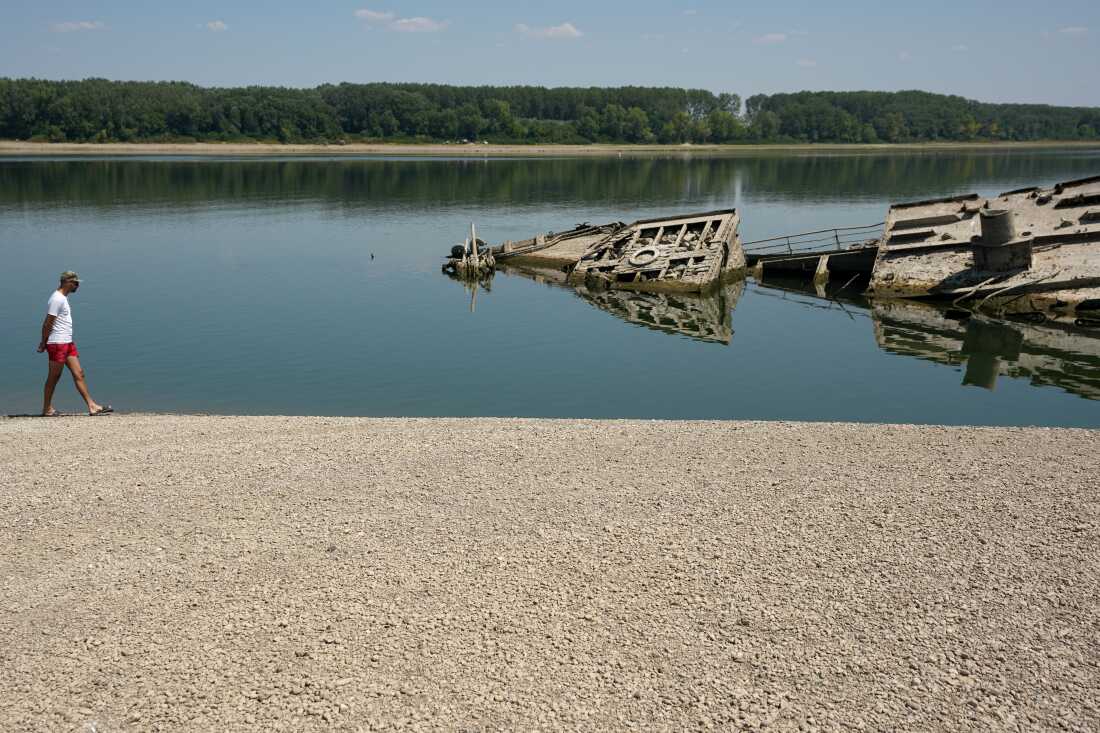 A man walks on the sandbank by the wreckage of a WWII German warship, emerged due to the drought, in front of Djerdap II, a large dam on the Danube River, between Romania and Serbia, near Prahovo, Serbia, Tuesday, Aug. 4, 2026.