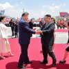 Two leaders wearing suits shake hands outdoors on a red carpet.
