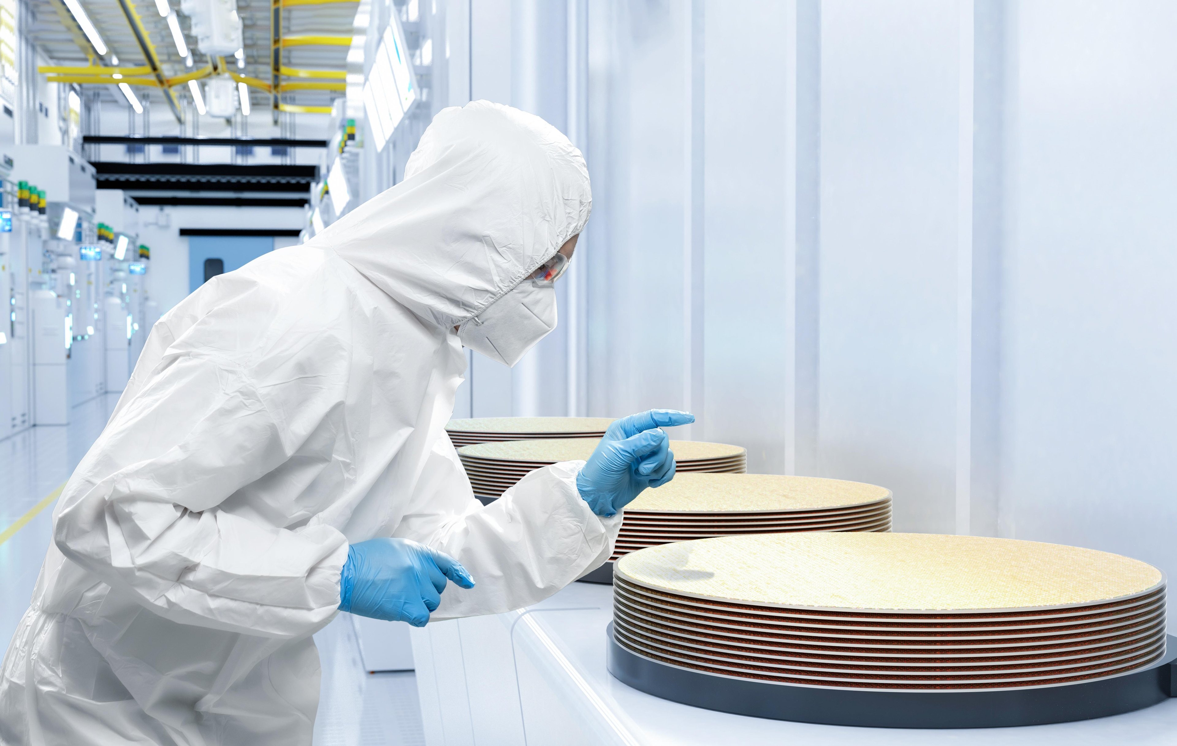 Engineer in cleanroom suit inspecting stacked silicon wafers in a semiconductor fabrication facility