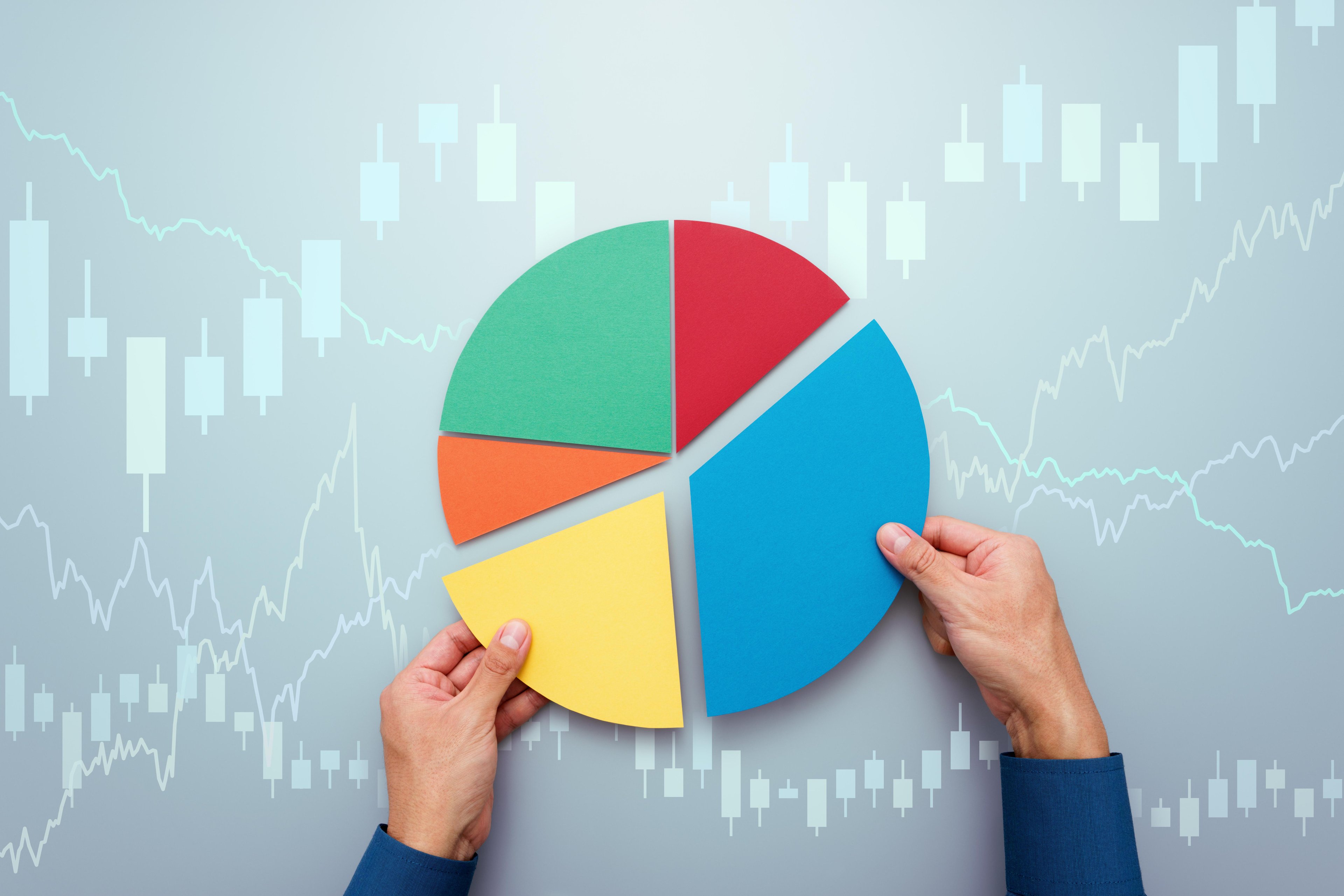 Hands arranging colorful pie chart segments over a background of financial stock market graphs
