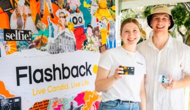 A young woman and man stand in front of a colorful collage backdrop branded "Flashback," each holding a small, rectangular camera.