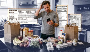Man in kitchen looking at his phone in a confused way.