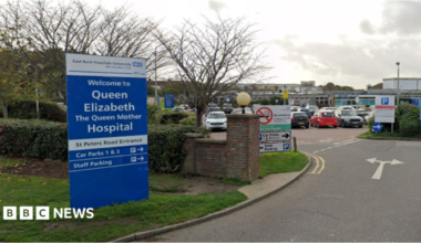 The main road entrance to the Queen Elizabeth the Queen Mother car park, with a blue sign to the left of the hospital's name