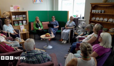 Patients sitting in a circle during one of the group sessions, with a crockery shelf to the right and a round table in the middle with a fruit bowl on it