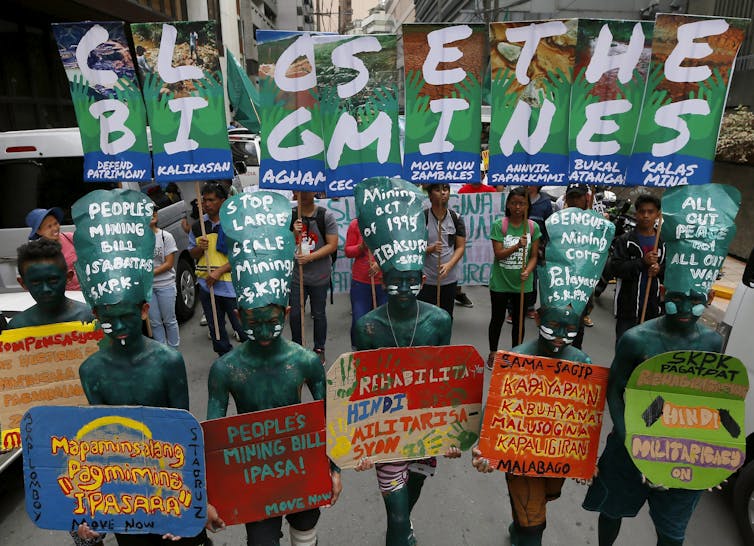 Protesters with their bodies painted green hold up colourful placards