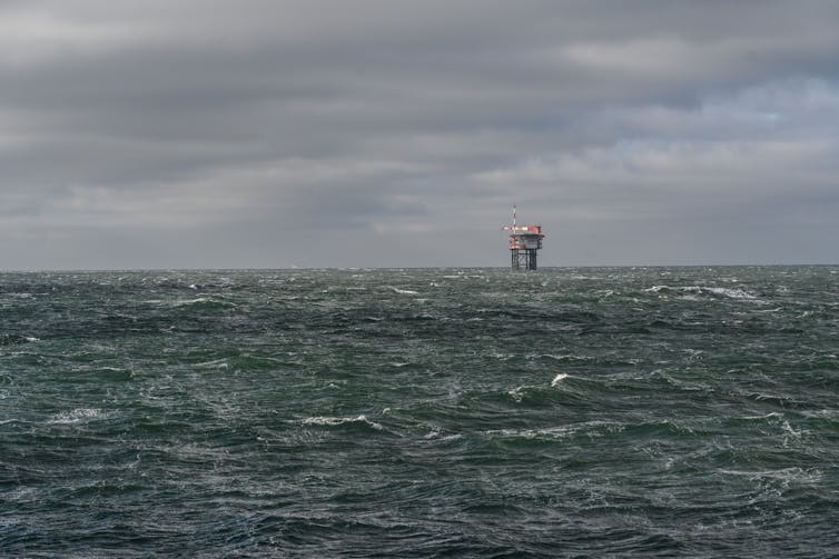 A large industrial tower rises out of a gray seascape.