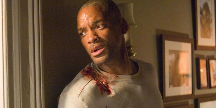 Will Smith hiding beside a window and looking out with blood on his shoulder in I Am Legend