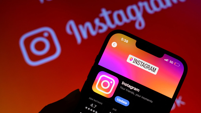 A smartphone displaying Instagram's App Store page sits in front of a blurred Instagram logo and wordmark.