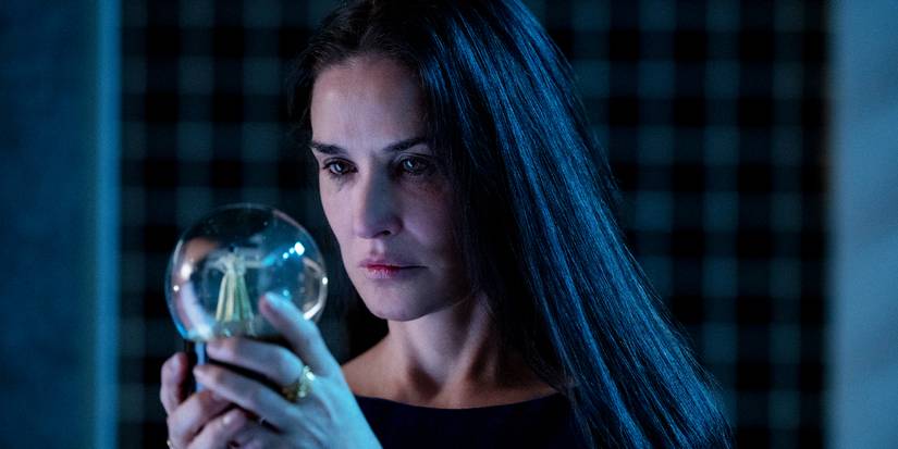 Demi Moore looking into a snow globe with a tense expression