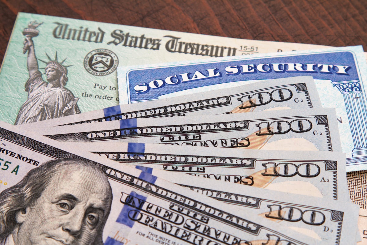 A U.S. Treasury check, a Social Security card, and U.S. currency spread over a wood surface.