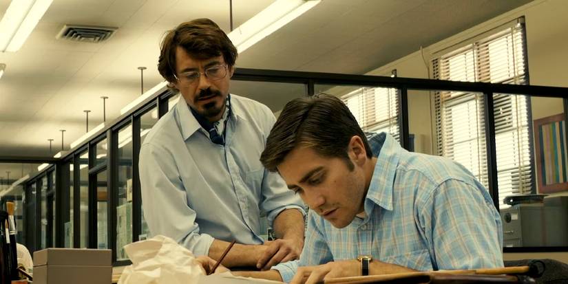 Robert Graysmith (Jake Gyllenhaal) hunchesover his desk while Paul Avery (Robert Downey Jr.) loiters casually behind him in 'Zodiac' (2007).