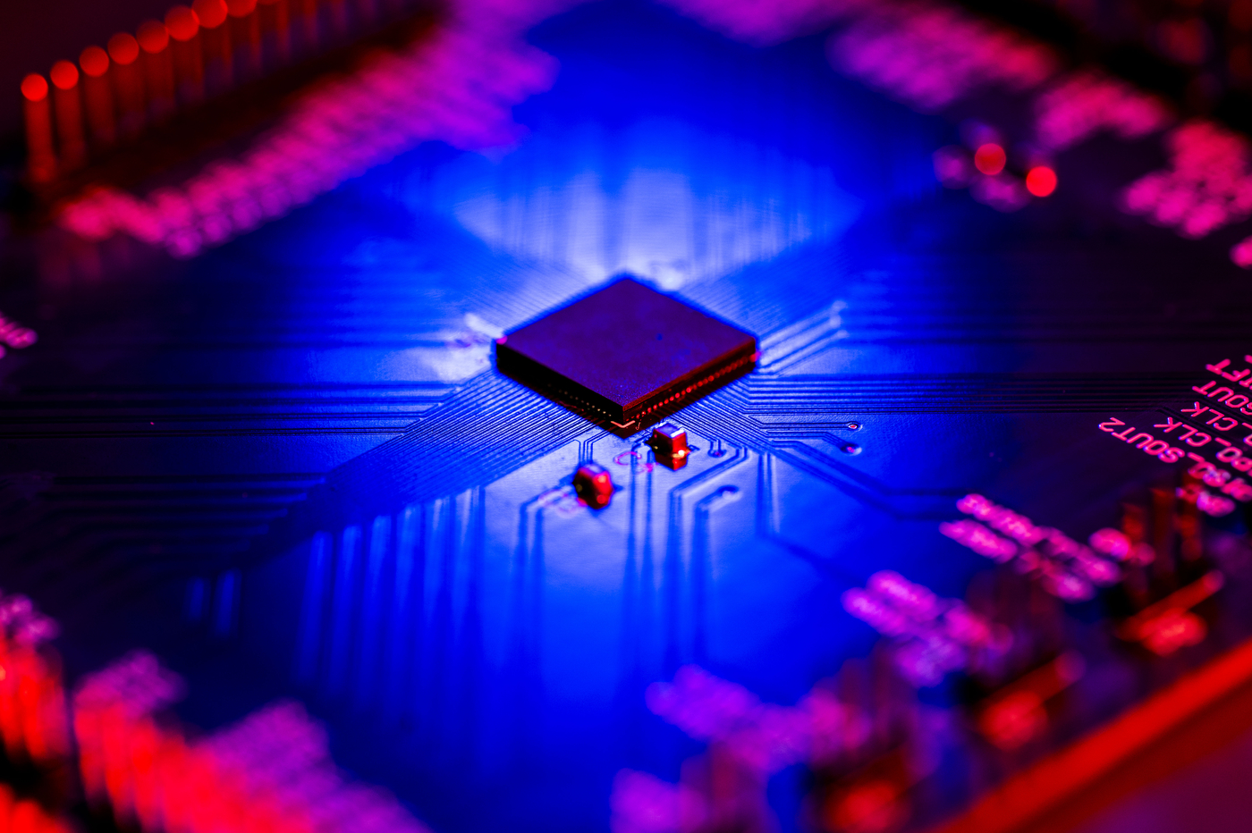 Close-up of a microchip on a circuit board lit in blue and red.
