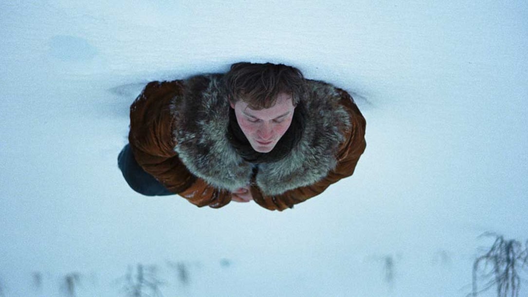 a young white man lays in the snow.