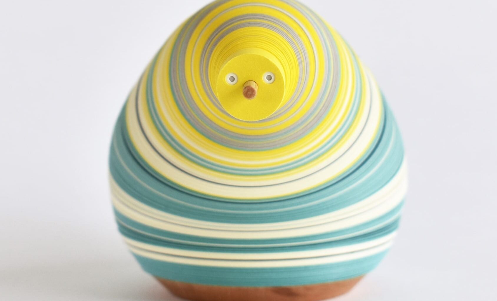 a small paper figure made from numerous layers of colored paper on a flexible central axis so that it looks like an anthropomorphized pear