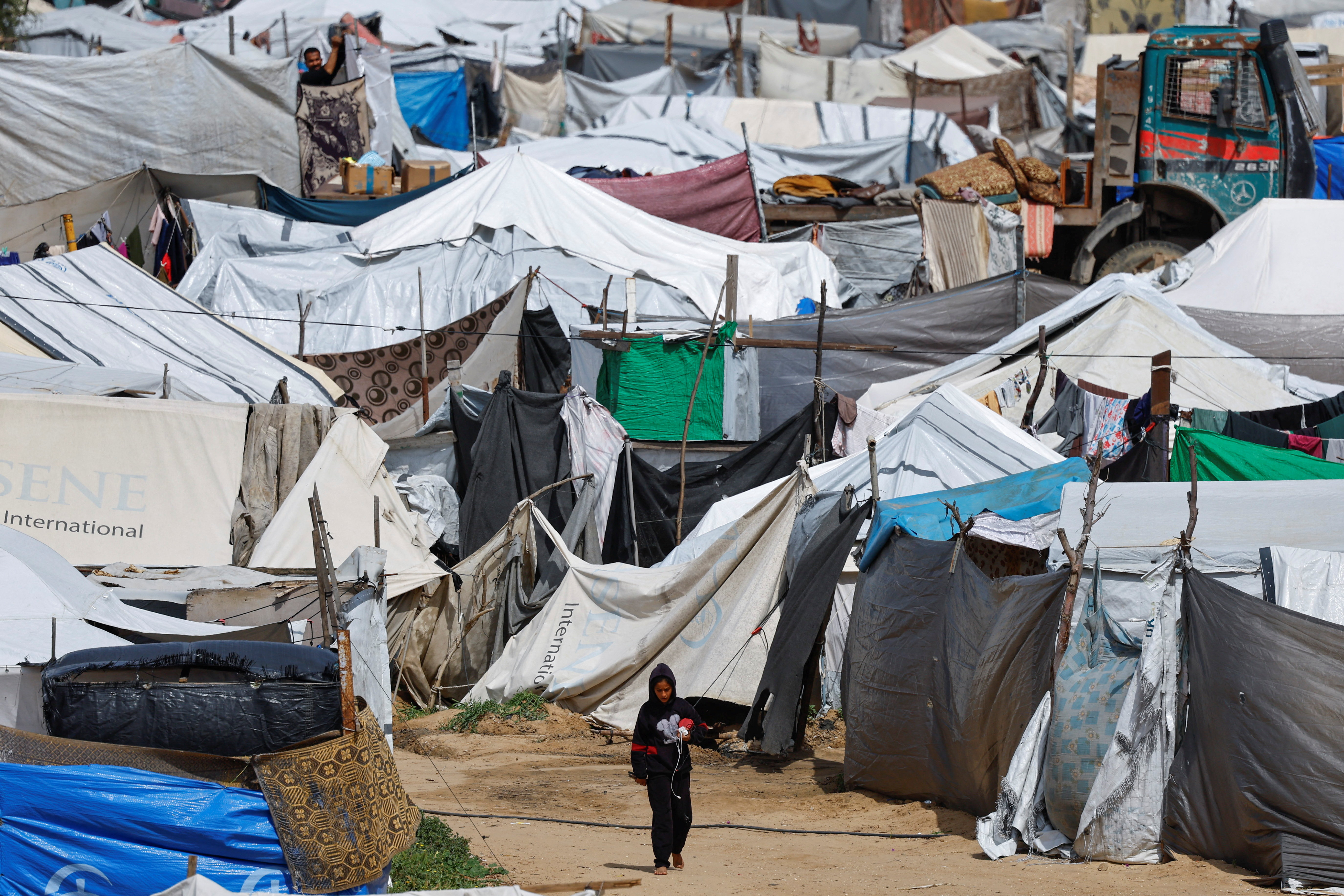 A Palestinian girl, displaced during the two-year Israeli offensive, walks at a tent camp sheltering displaced families, in Nuseirat, central Gaza Strip, March 25, 2026. (REUTERS/Mahmoud Issa)