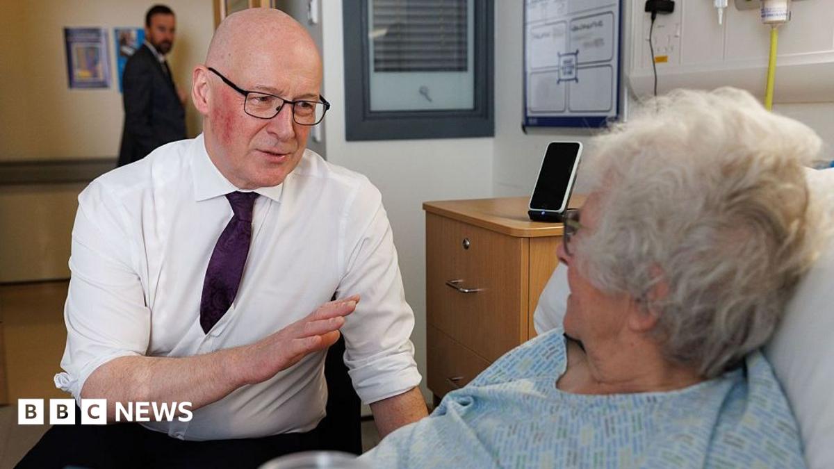 John Swinney talking to a female hospital patient who is in bed.