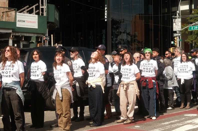 Several protestors, wearing white t-shirts that read "Fund People Not Bombs," yell as they get arrested by the NYPD officers.