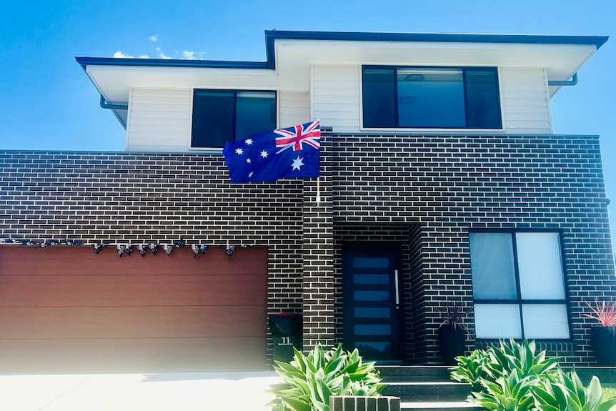 A brick house with an Australian flag attached near the front door and little flags running over the top of garage door.