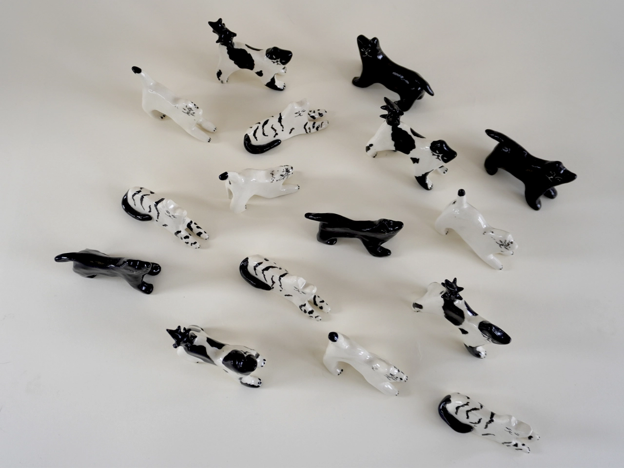 Collection of black and white ceramic cat figurines in various striped and spotted patterns arranged on a neutral surface