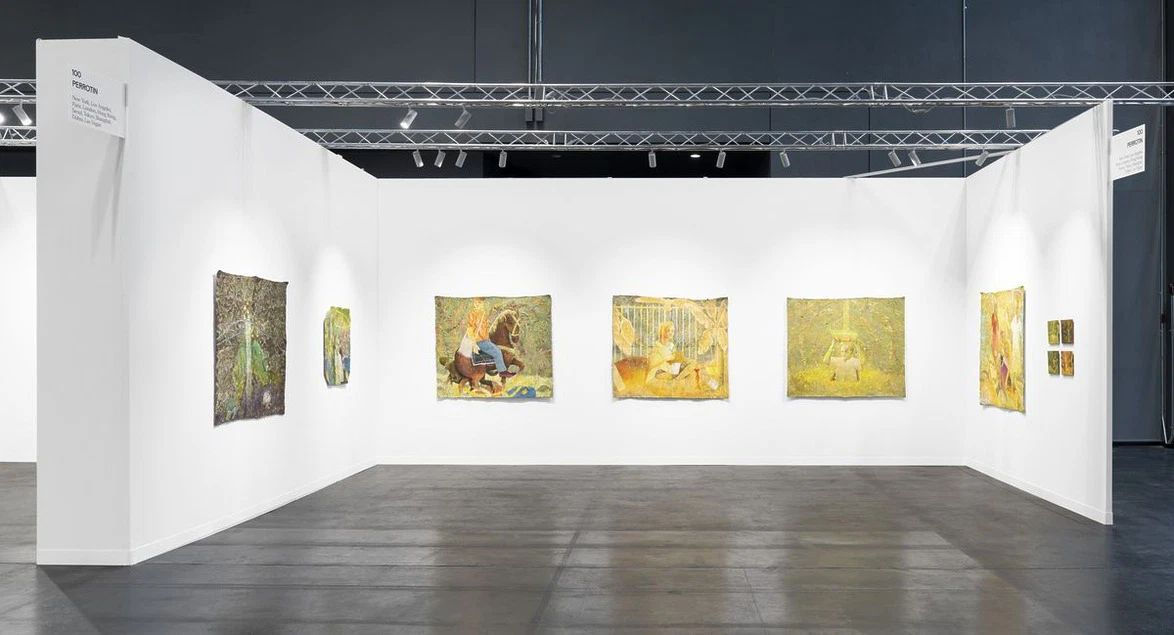 Art gallery exhibition with paintings displayed on white walls under bright lighting.