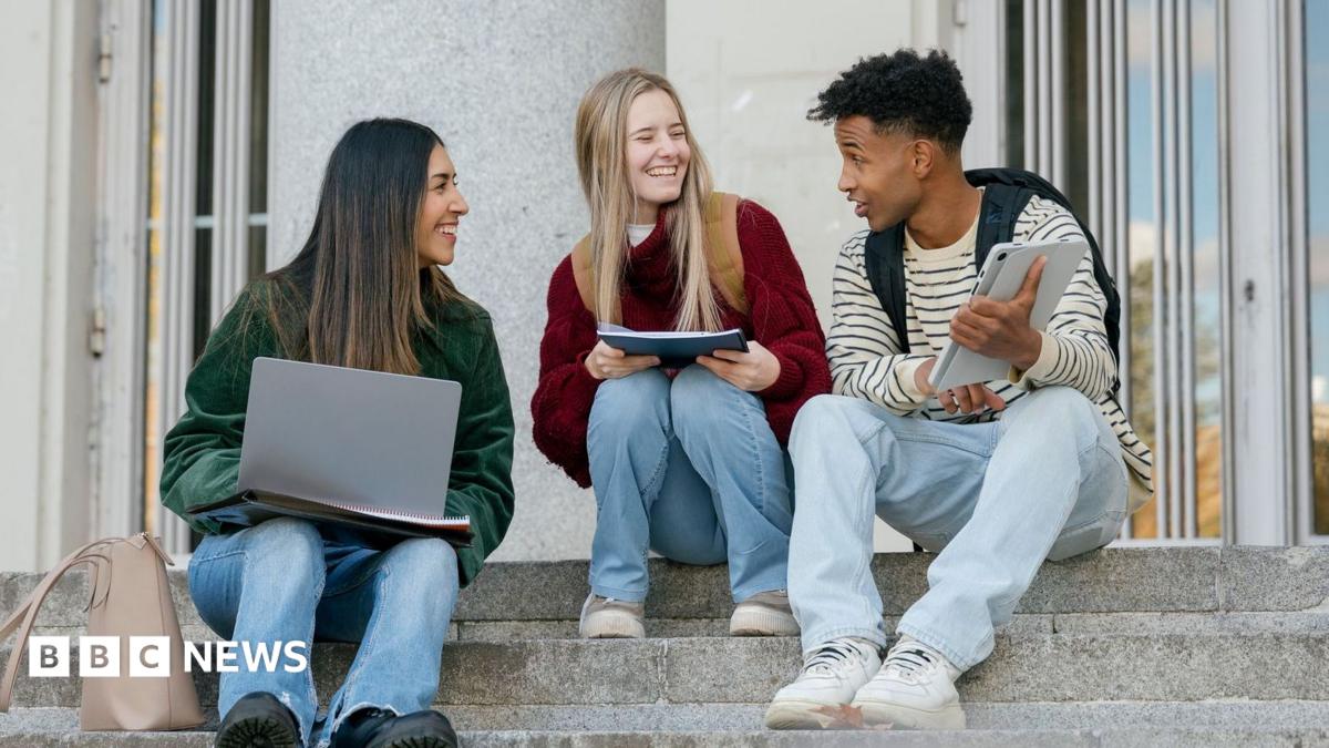 Three university students sitting on concrete stairs, talking and smiling while looking at a digital tablet and laptop. There are two women to the left both looking at a male student to the right.