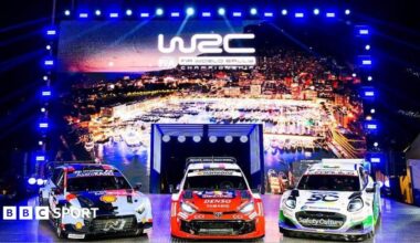 Three rally cars in front of a lit up sign featuring the World Rally Championship logo