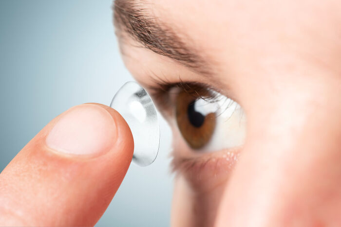 Close-up of a person inserting a contact lens into their eye, a common behavior patients lie about during medical exams.