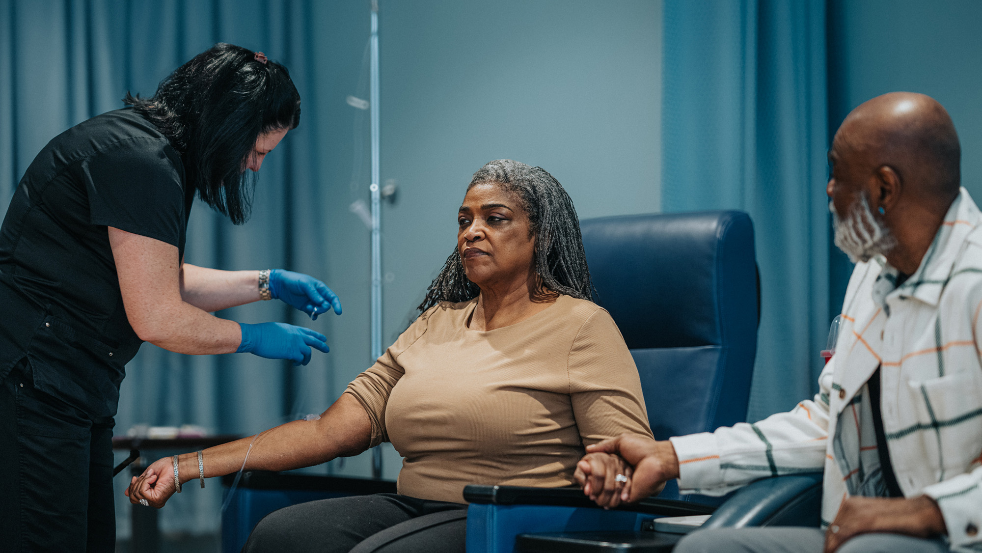 A woman sitting in a medical chair receives an IV.