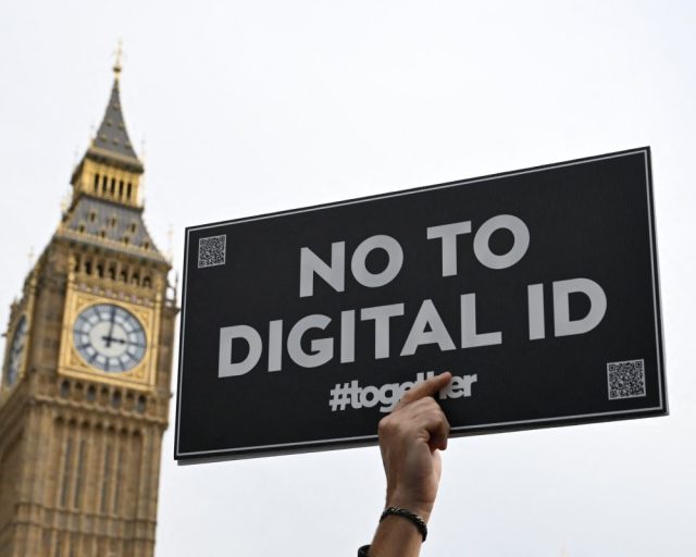 A demonstrator holds up a placard outside The Palace of Westminster during a march against the implementation of digital ID cards, in central London on October 18, 2025. UK Prime Minister Keir Starmer on September 26, 2025, announced plans for a new nationwide digital ID in a bid to curb illegal migration, but the move faces strong opposition in a country that has long resisted identity cards. The new digital ID will be held on people's phones and there will be no requirement for individuals to carry or be asked to produce it, the government said. A petition demanding that ID cards not be introduced has collected more than 2,889,412 signatures. (Photo by Chris J Ratcliffe / AFP) (Photo by CHRIS J RATCLIFFE/AFP via Getty Images)