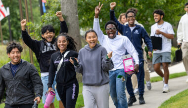 Students smile and raise their arms while walking on campus