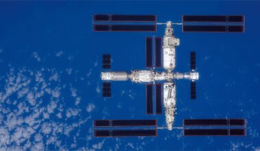 a large T-shaped space station is seen from above with Earth below it