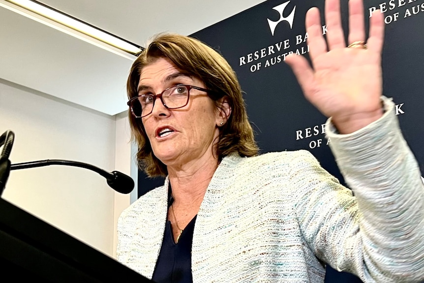 RBA governor Michele Bullock holds her hand up while speaking at a press conference.
