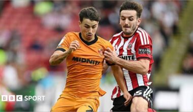 Liam Kitching in a red and white striped Sheffield United shirt battles for the ball against Wolves