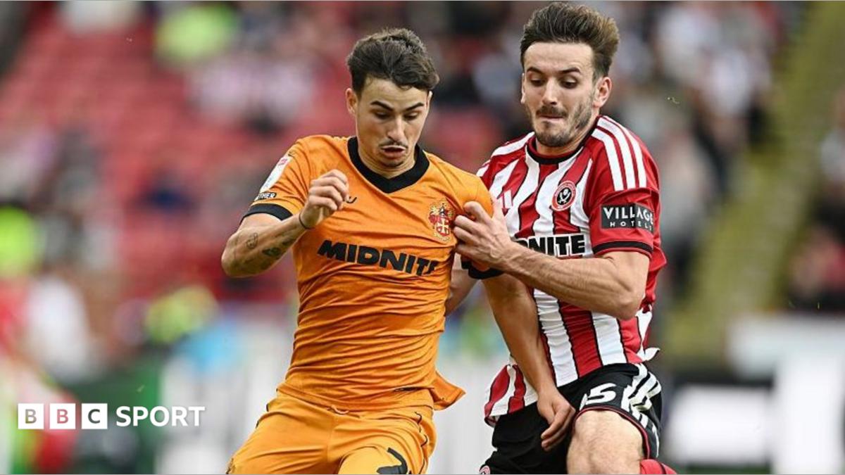 Liam Kitching in a red and white striped Sheffield United shirt battles for the ball against Wolves