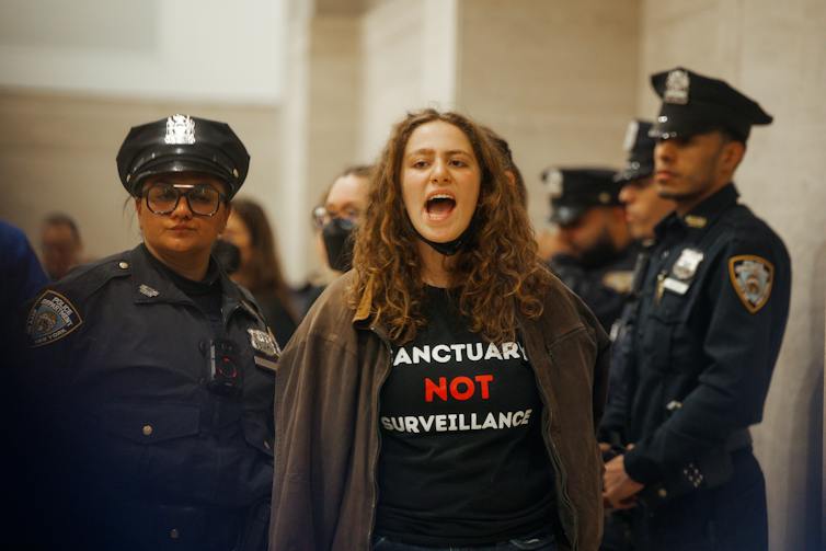 A woman being arrested by uniformed police, as she shouts.